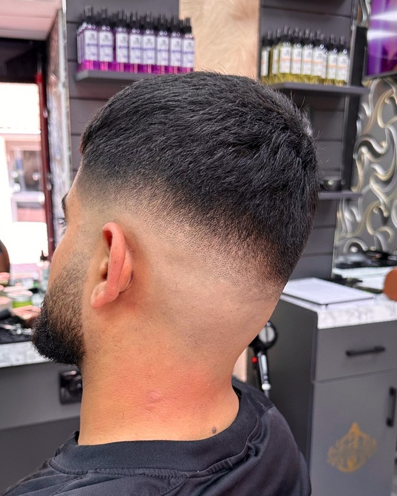 Klant met een strakke skin fade en een verzorgde baard, voor de spiegel in de zaak